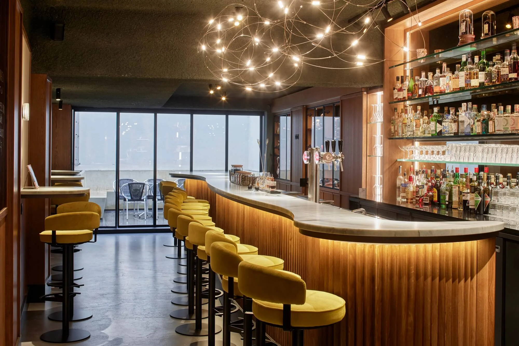 A wide view of the bar from the opposite end, with warm floor reflections and the mustard-yellow stools